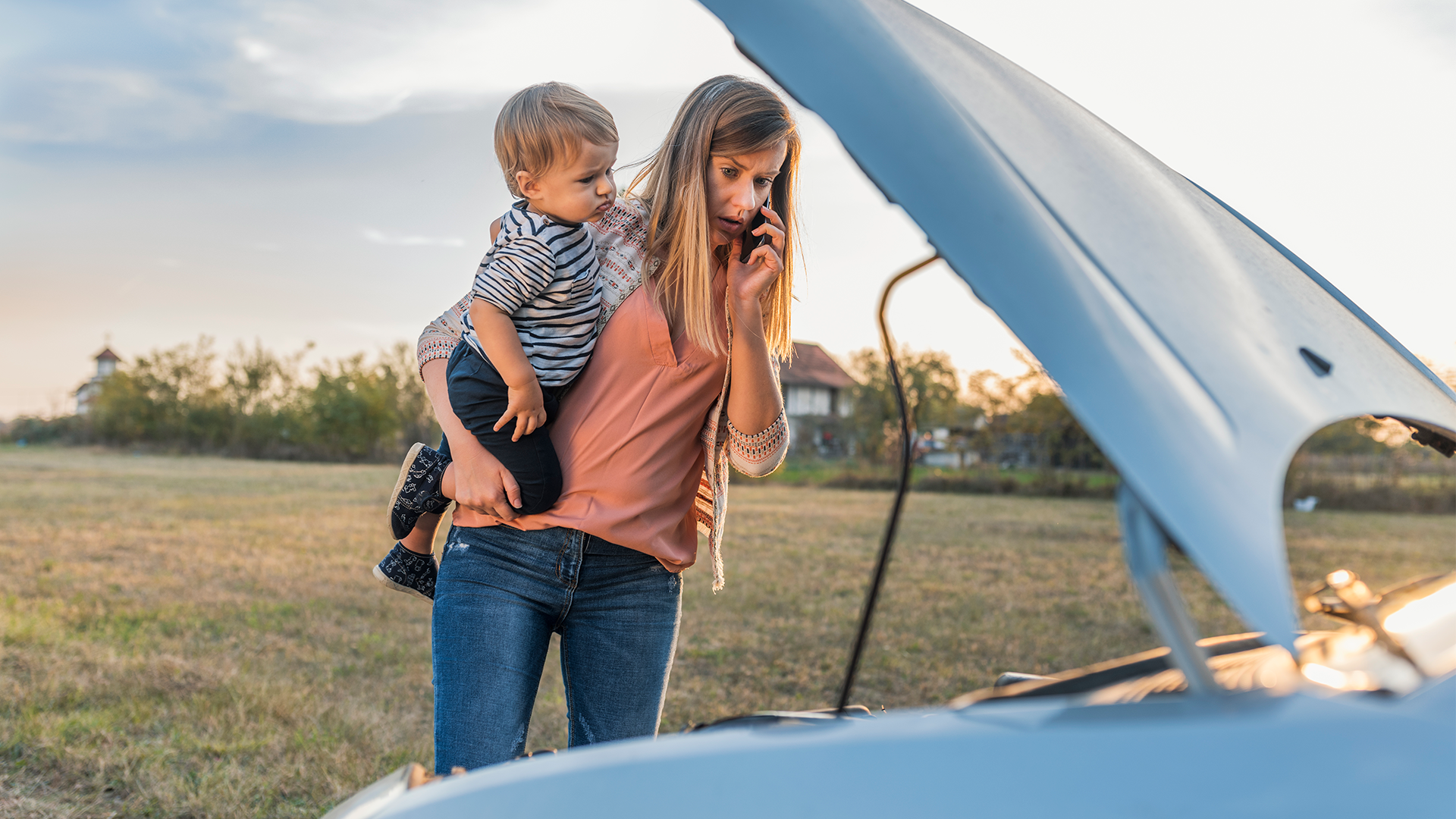 Mother calling roadside assistance for a car while holding a child