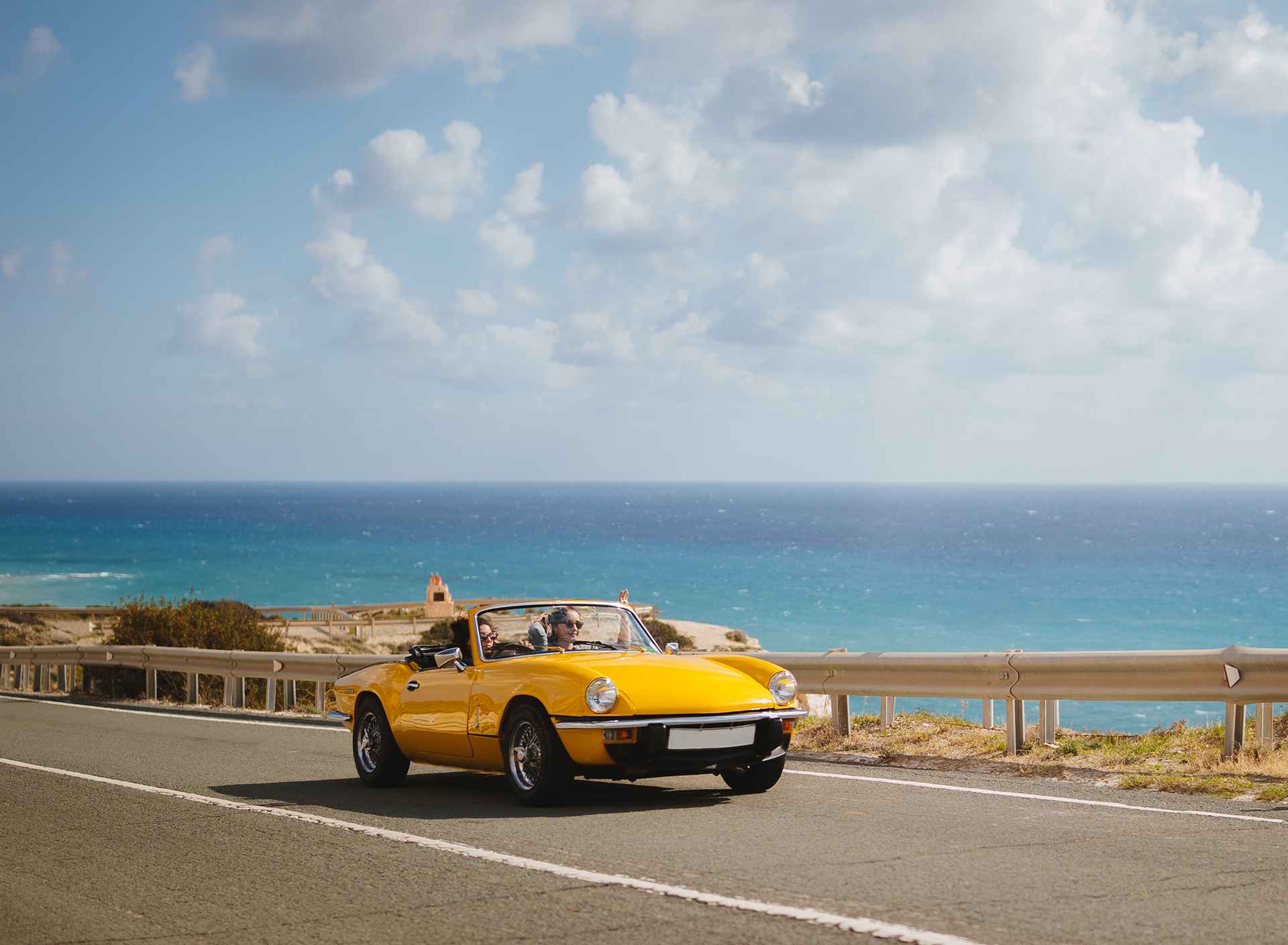 classic car driving with a beach in the background