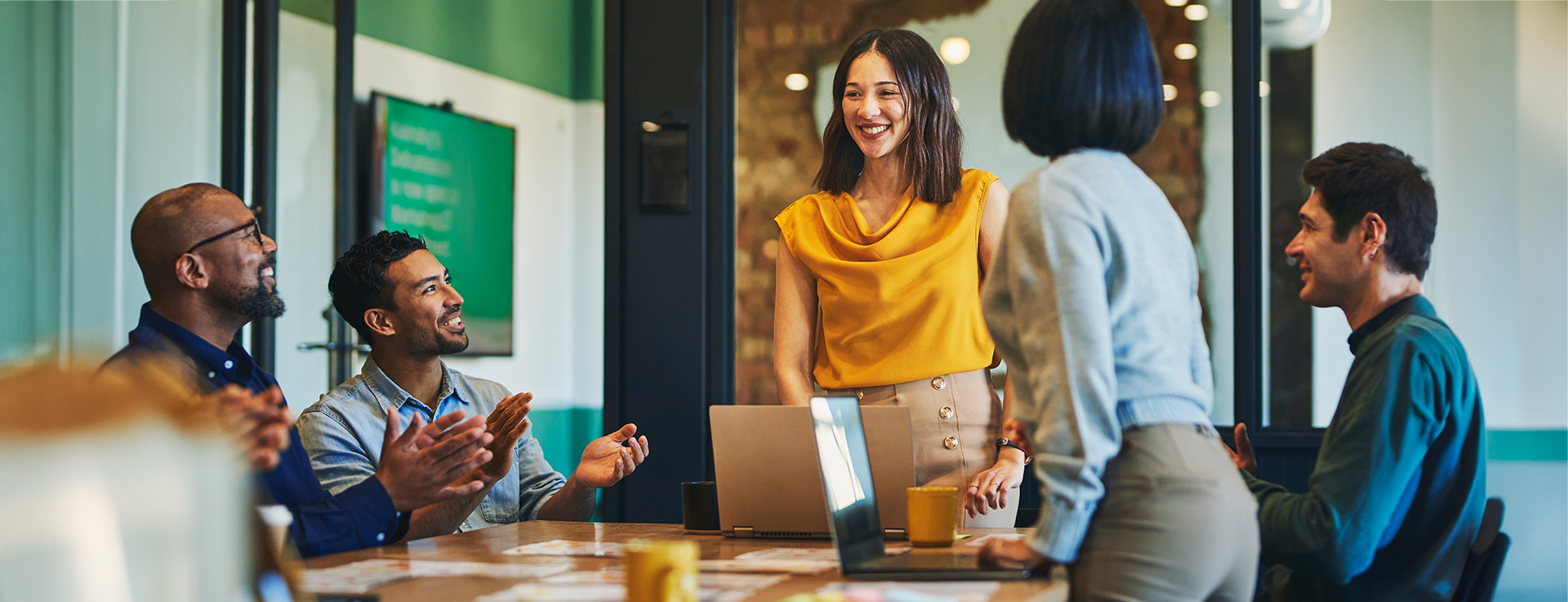 Businesswoman standing and smiling proudly at supportive colleagues clapping her for closing business deal in boardroom